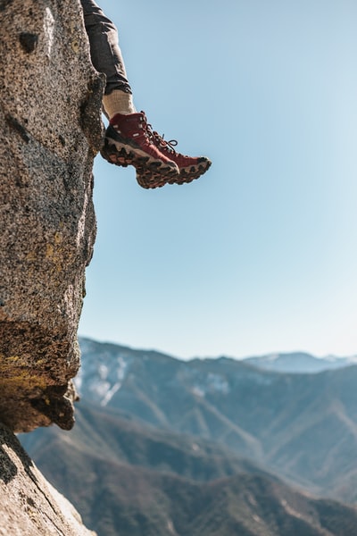 白天穿着红白相间的登山鞋坐在山对面的岩壁上的人